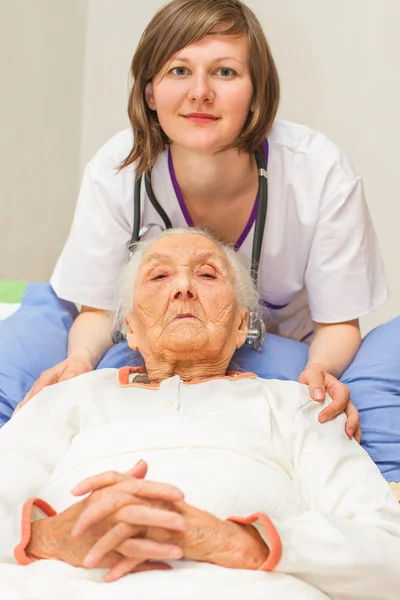 Young nurse caregiving an old lady lying in bed