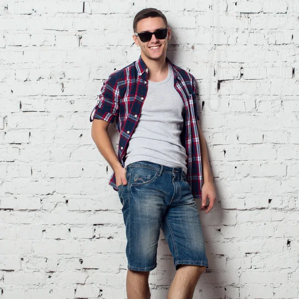 Handsome stylish young man in jeans shorts and shirt. Attractive hipster  with a bristle,sunglasses