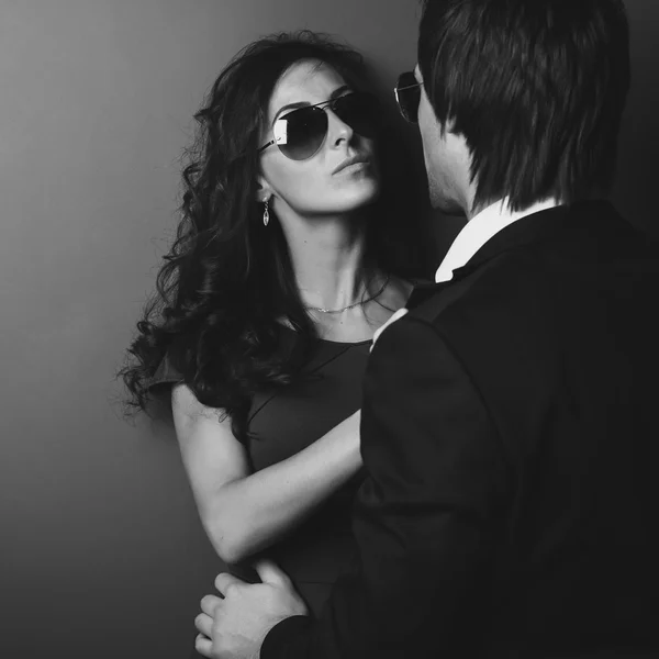 Stunning girl in glasses next to wall and her man front of her. Black white