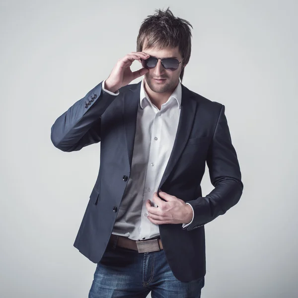 Fashion portrait of the young beautiful man posing in sun glasses over gray background