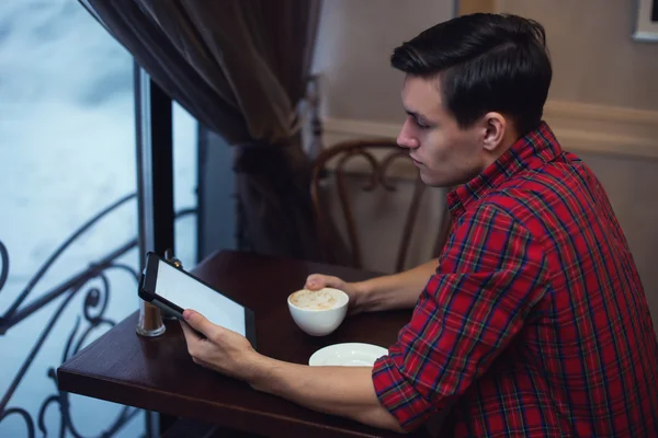 Handsome young man reading news using tablet while drinking coffee in a cafe sitting backside to the camera