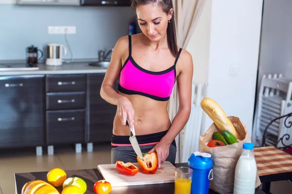 Athletic active sportive woman standing in kitchen with a knife her hand prepares healthy food fresh fruits milk bread on table