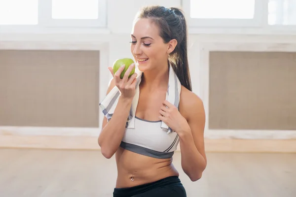 Active athletic sportive woman with towel in sport outfit holding apple after the training.