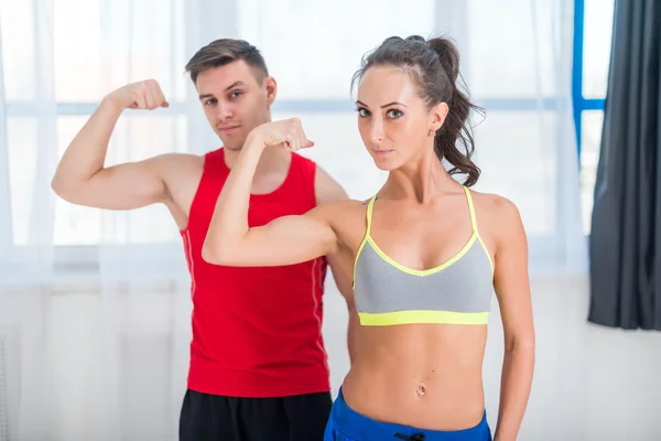 Active athletic sportive woman girl and man showing their muscles biceps healthy lifestyle looking at camera
