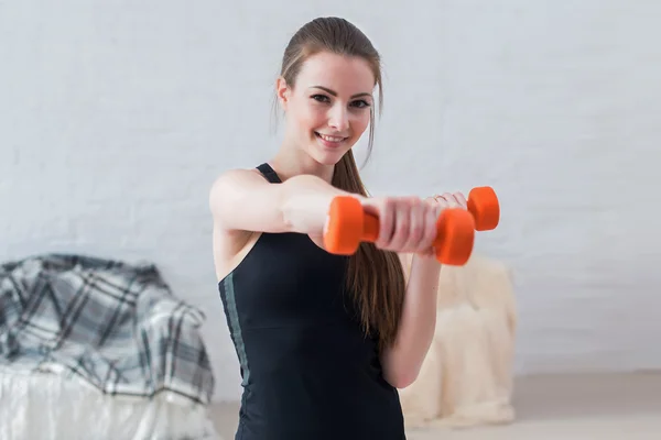 Active sportive athletic woman boxing dumbbells pumping up muscles towards camera in bright room concept fitness sport training lifestyle