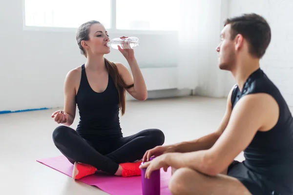 Sport connecting people friends relaxing after workout girl drinking water and man Side view of young couple in sports clothing sitting talking conversing.