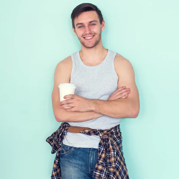 Portrait young man arms crossed holding paper cup of coffee city street casual urban style looking at camera standing near wall.