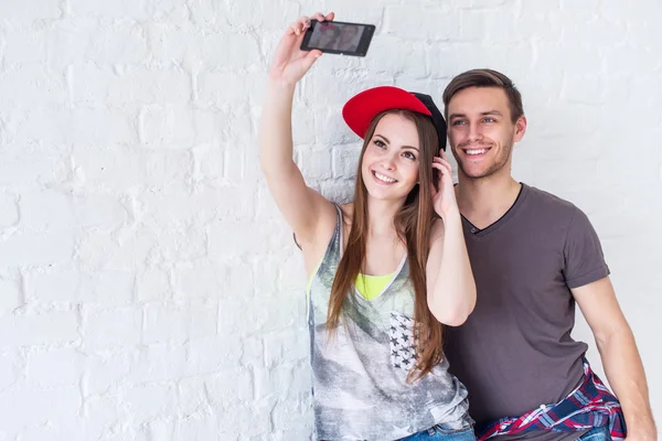 Couple friends taking selfie self-portrait picture photo together with camera or smartphone wearing summer clothes street urban casual style having fun.