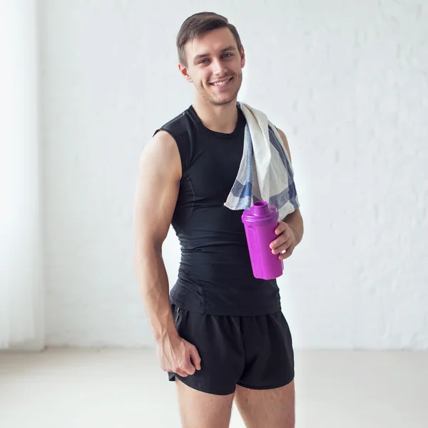 Portrait of a athletic smiling man after doing exercises sportsman holding towel and shaker protein cocktail or bottle with water.