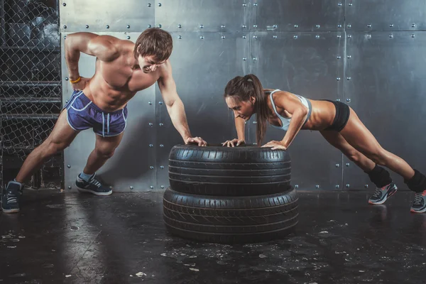Sportswomen. Fit sporty woman and man doing push ups on tire strength power training concept crossfit fitness workout sport lifestyle.