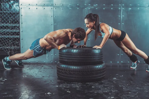 Sportswomen. Fit sporty woman and man doing push ups on tire strength power training concept crossfit fitness workout sport lifestyle.