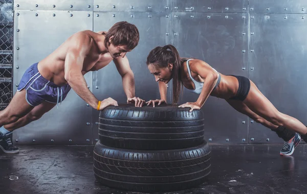 Sportsmen. Fit sporty woman and man doing push ups on tire strength power training concept crossfit fitness workout sport lifestyle.