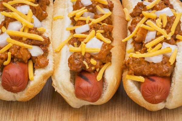 Three delicious chili hot dogs on a wood cutting board