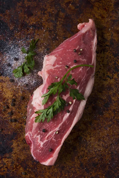 Raw steak top view with parsley leaves peppercorns and salt on a rustic background