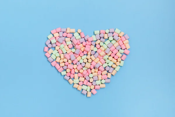 Pastel marshmallow in the shape of a heart on a blue background overhead shot