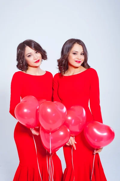 Two young beautiful women in a long red dress with balloons