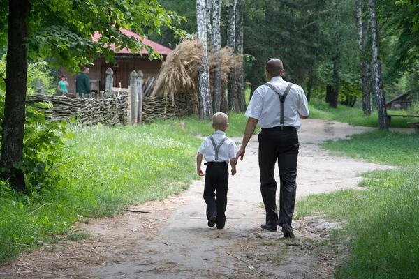 Rear view of father and son holding hands while walking in forest
