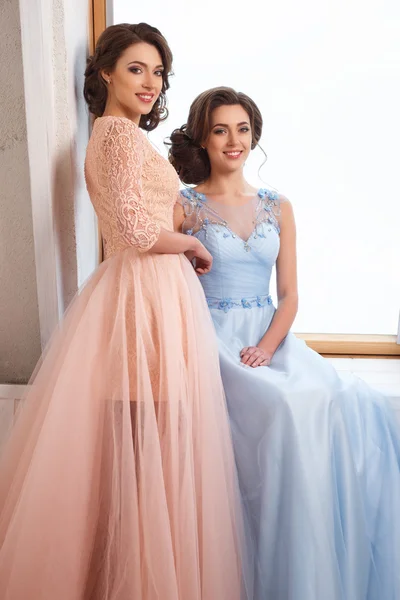 Two beautiful twins young women in luxury dresses, pastel colors. Beauty fashion portrait