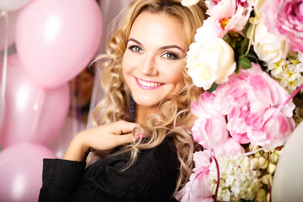 Close-up portrait of beautiful curly young woman in a room with many pink and white air balloons and flowers. Beauty fashion portrait