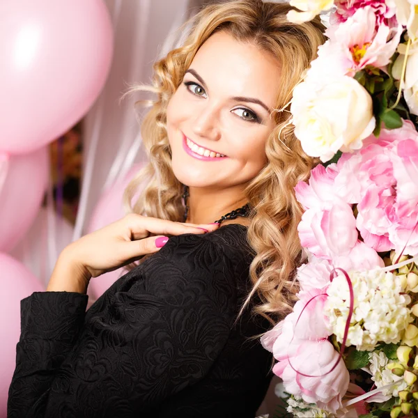 Close-up portrait of beautiful curly young woman in a room with many pink and white air balloons and flowers. Beauty fashion portrait