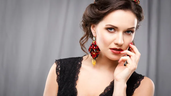 Elegant young woman with perfect makeup and hair style in a black dress with diadem and earrings. Beauty fashion portrait with accessories