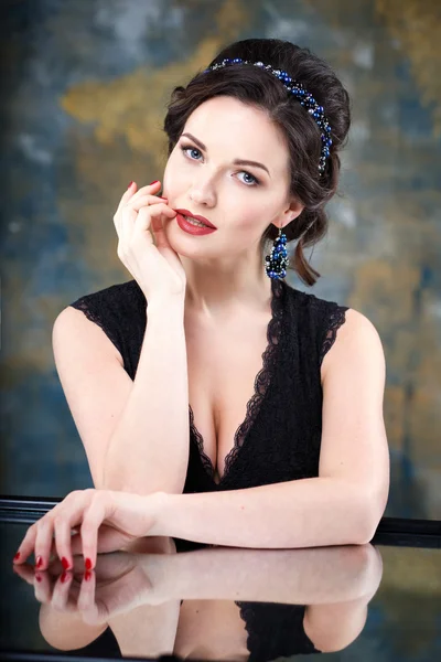 Elegant young woman with perfect makeup and hair style in a black dress with diadem and earrings. Beauty fashion portrait with accessories