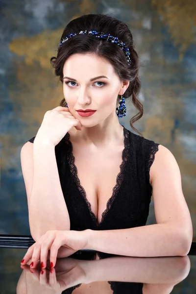 Elegant young woman with perfect makeup and hair style in a black dress with diadem and earrings. Beauty fashion portrait with accessories