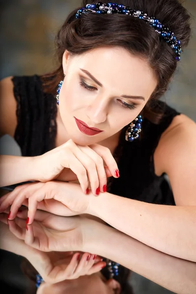 Elegant young woman with perfect makeup and hair style in a black dress with diadem and earrings. Beauty fashion portrait with accessories