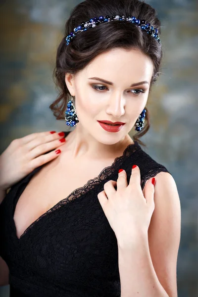 Elegant young woman with perfect makeup and hair style in a black dress with diadem and earrings. Beauty fashion portrait with accessories