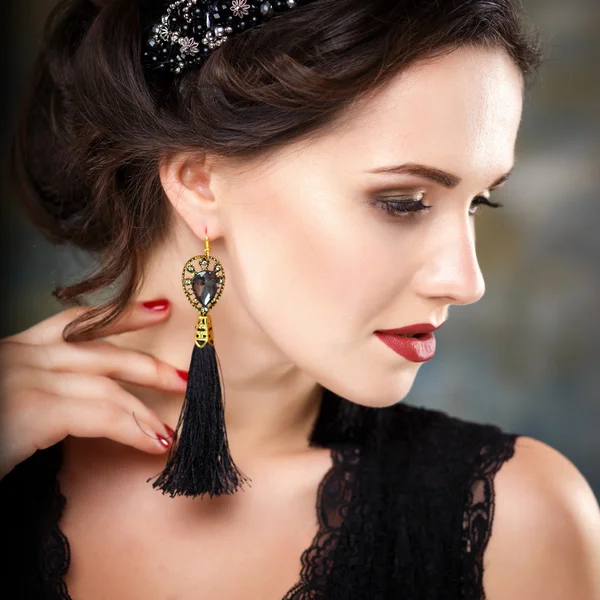 Elegant young woman with perfect makeup and hair style in a black dress with diadem and earrings. Beauty fashion portrait with accessories