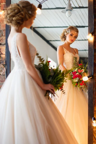 Beautiful blonde bride in gorgeous luxury dress in a loft space with a mirror and garland of lamps. Modern wedding photo