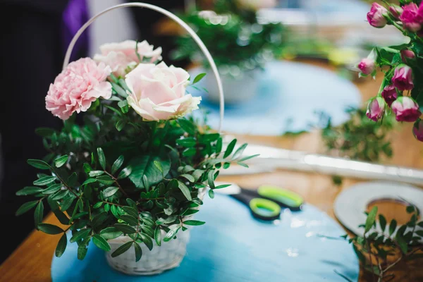 Florist workplace: pretty bouquet in a basket on a background of flowers and accessories. soft focus