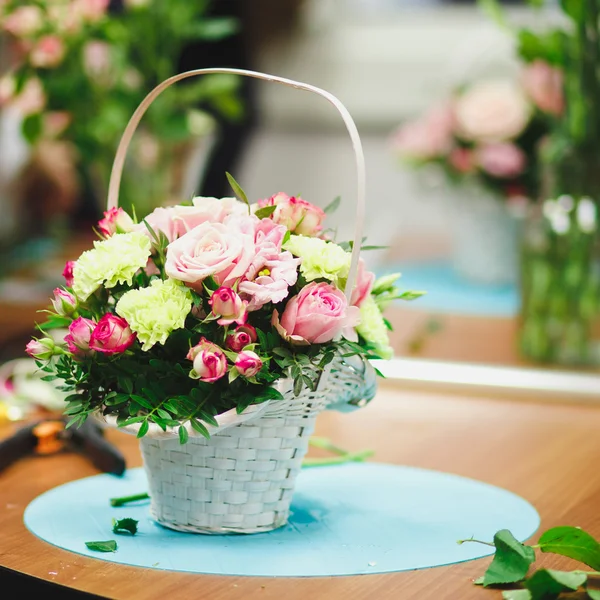 Florist workplace: pretty bouquet in a basket on a background of flowers and accessories. soft focus