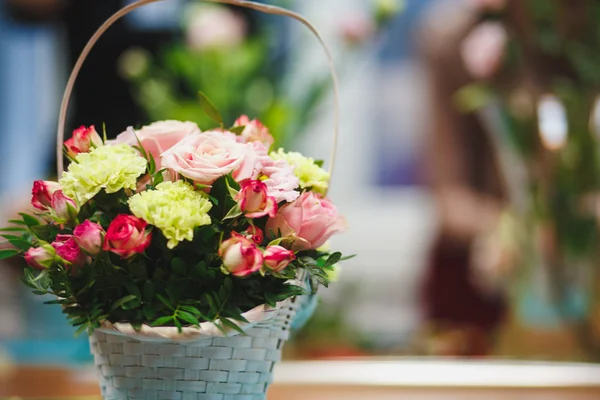 Florist workplace: pretty bouquet in a basket on a background of flowers and accessories. soft focus