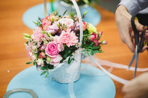 Florist workplace: pretty bouquet in a basket on a background of flowers and accessories. soft focus
