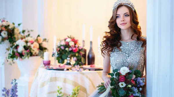 Beautiful young lady in a luxury dress in elegant interior with a bouquet of flowers