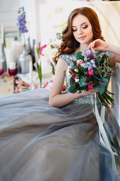 Beautiful young lady in a luxury dress in elegant interior with a bouquet of flowers