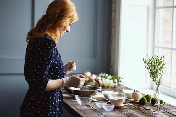 Young woman prepare bath bombs. Ingredients and floral decor on a wooden vintage table.