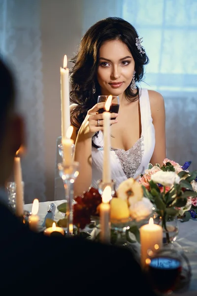 Close-up portrait of beautiful brunette bride, sitting by a table with decor and candles with her groom