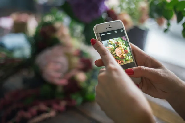 Florist at work: pretty young blond woman making photo on her mobile phone (smart phone)