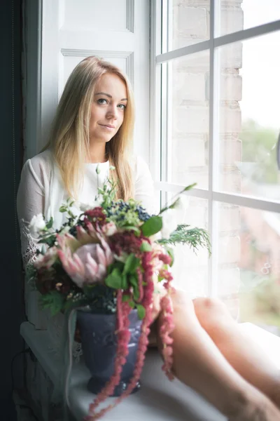 Florist at work: pretty young blond woman making fashion modern bouquet of different flowers