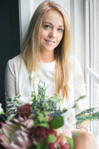 Florist at work: pretty young blond woman making fashion modern bouquet of different flowers