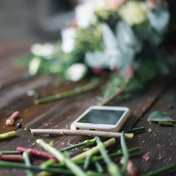 Florist workplace: mobile phone (smart phone) and flowers and accessories on a vintage wooden table. soft focus