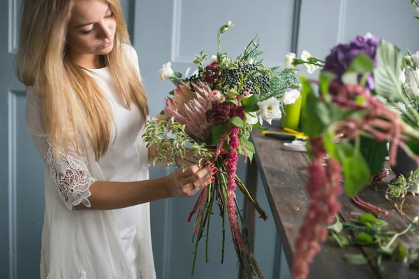 Florist at work: pretty young blond woman making fashion modern bouquet of different flowers