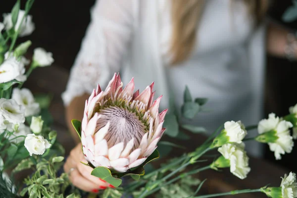 Florist at work: pretty young blond woman making fashion modern bouquet of different flowers