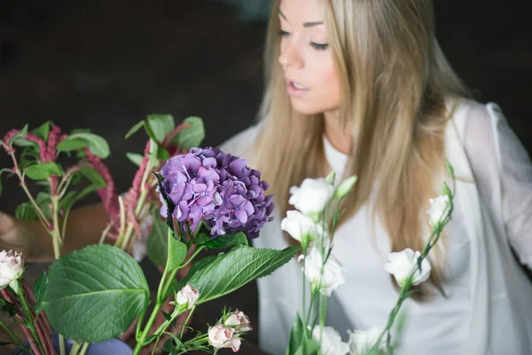 Florist at work: pretty young blond woman making fashion modern bouquet of different flowers