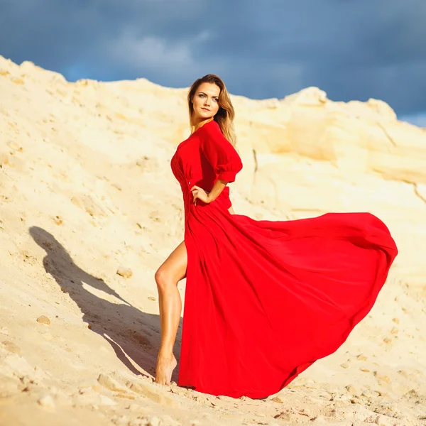 Gorgeous red head young woman in long red dress in a dessert. Sandy canyon. Fashion style