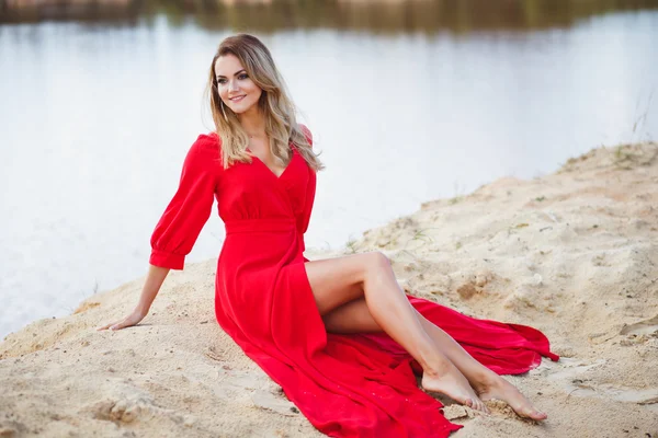 Gorgeous red head young woman in long red dress on a background of a lake. Sandy canyon. Fashion style