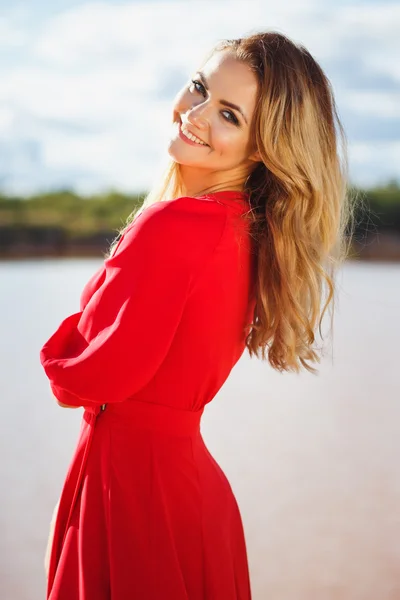 Gorgeous red head young woman in long red dress on a background of a lake. Sandy canyon. Fashion style
