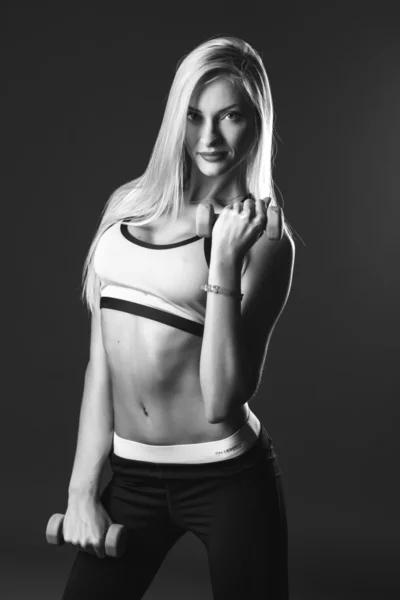 Close-up portrait of sport young blonde woman with dumbbells over dark background isolated. Fitness model. Black and white photo